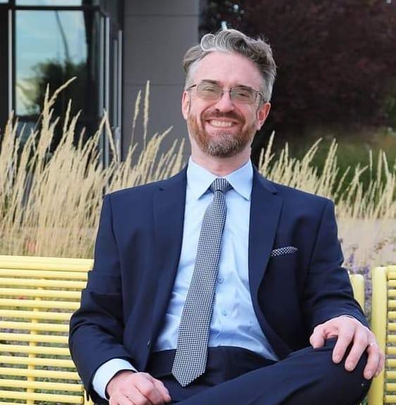 Pastor Charles Wiese seated outdoors in a navy suit and tie.